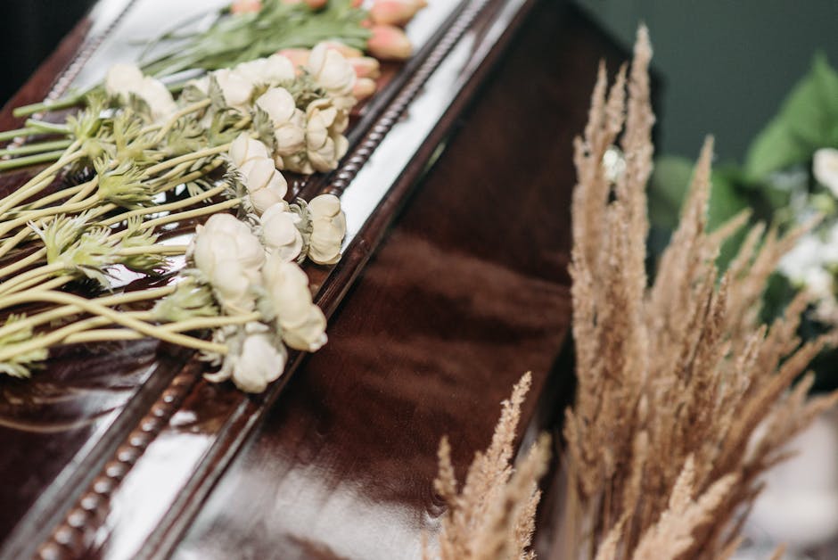 A close-up of a wooden table with a partially visible elegant floral arrangement, featuring white roses and pale pink tulips with waved green stems, laid across the surface. To the right, a bundle of 